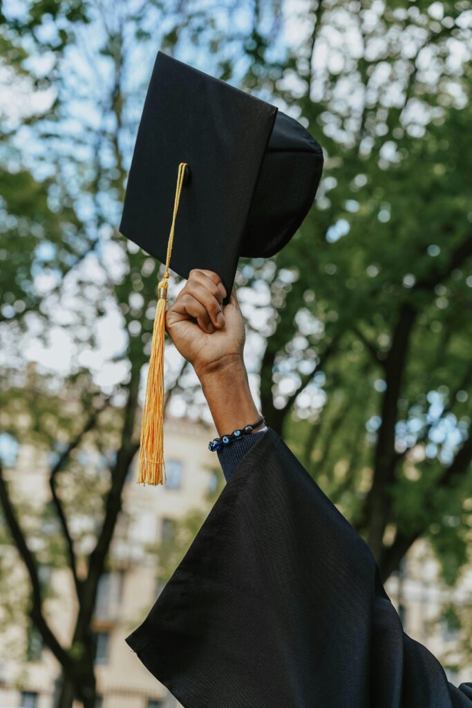 pexels photo 8093033 8093033 A close-up of a hand raising a graduation cap in celebration among trees.